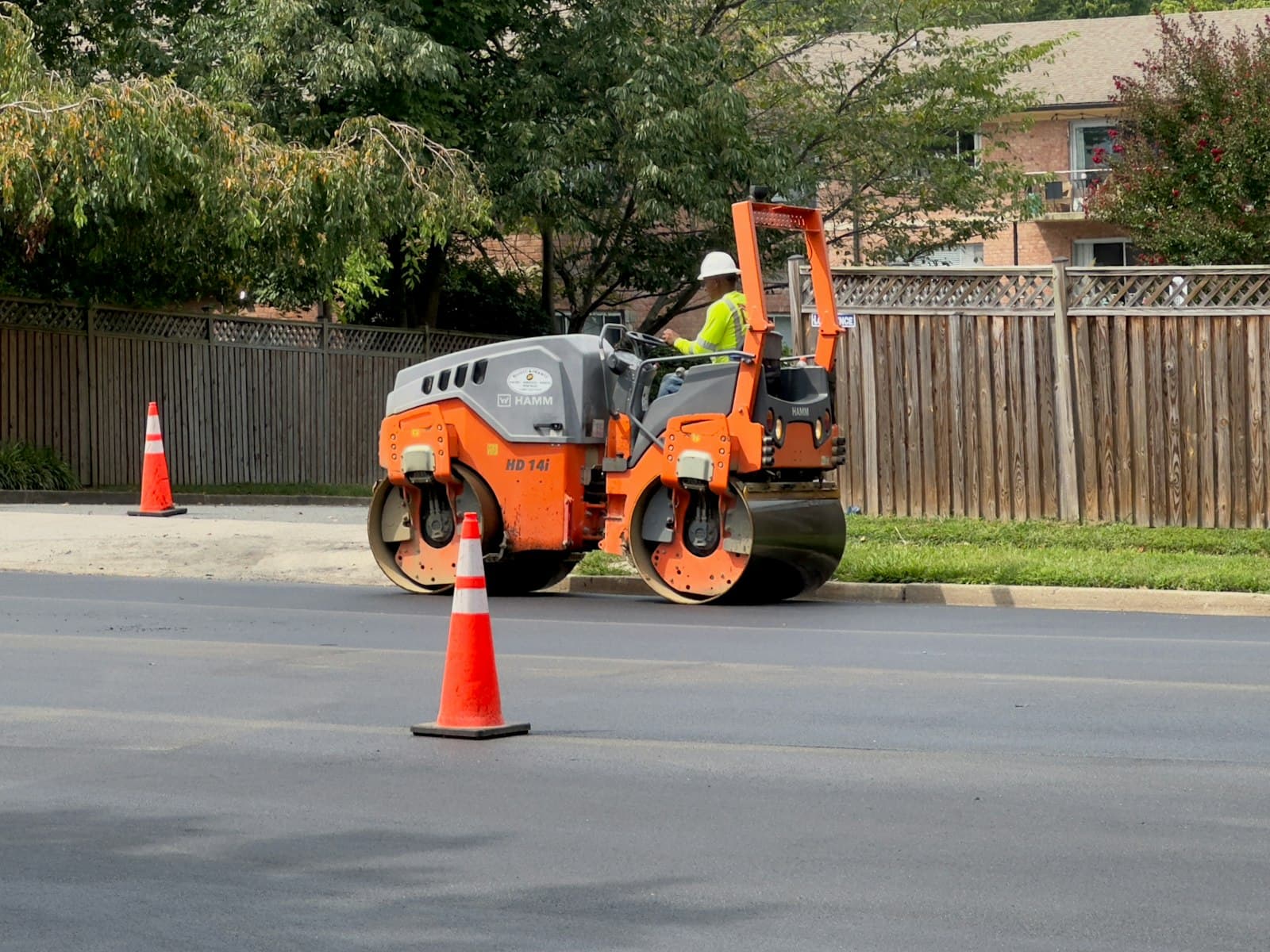 Roller compactor finishing fresh asphalt on a residential street