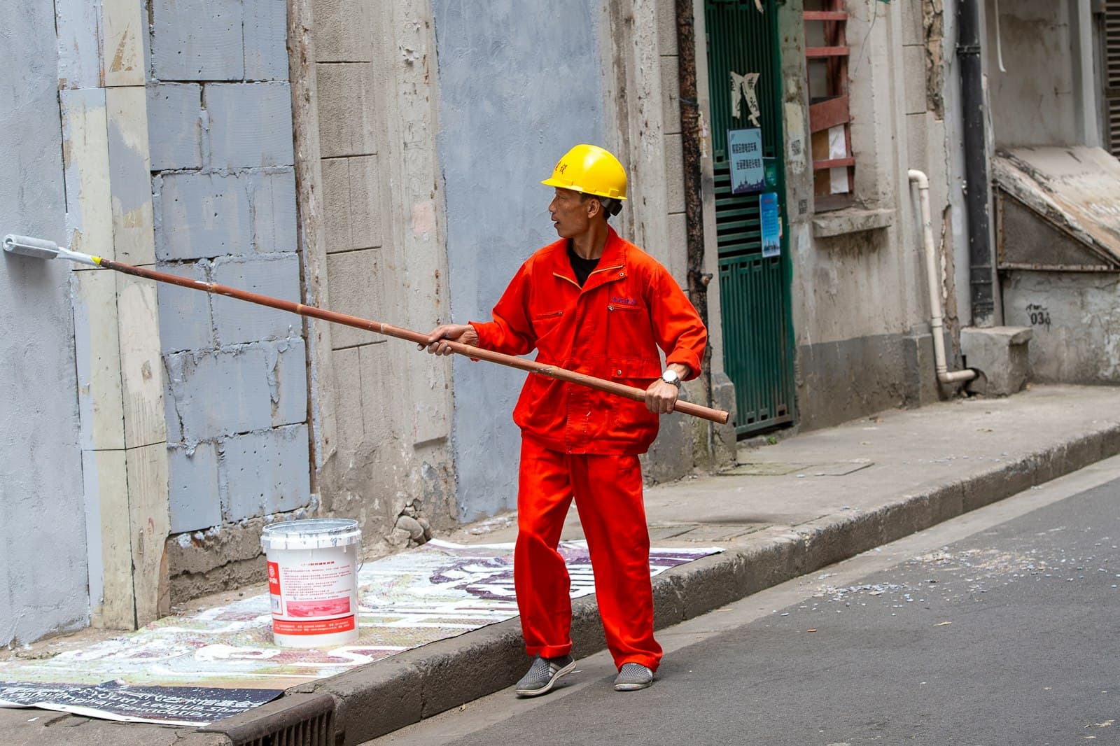 Painter in work gear rolling fresh paint onto a building exterior