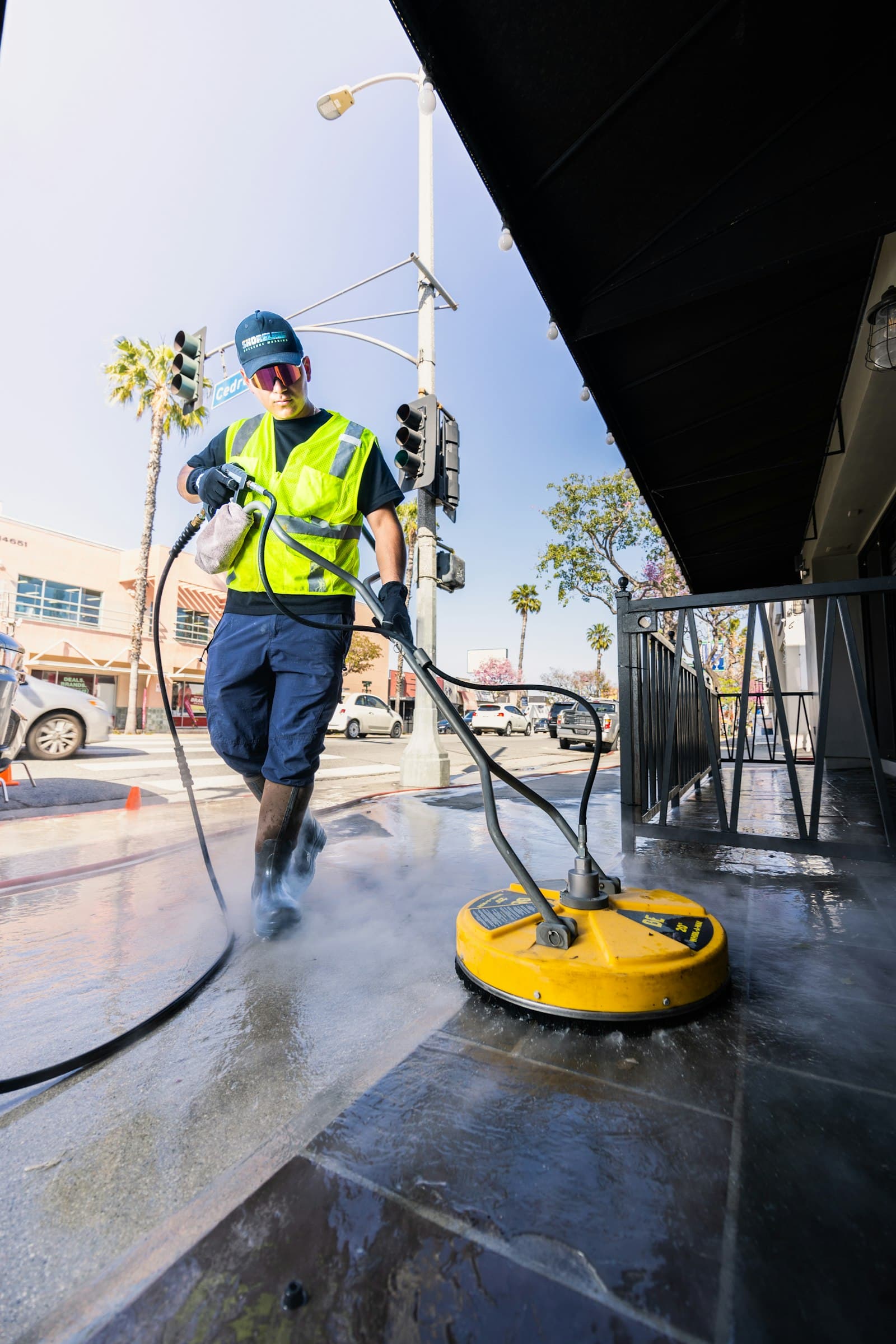 Technician in a safety vest power washing pavement with a surface cleaner